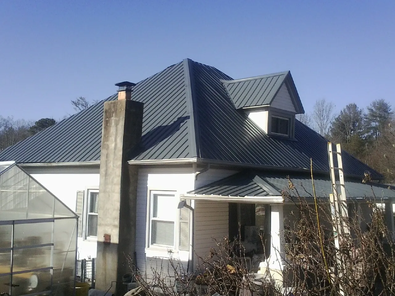 Dark blue standing seam metal roof on a white farmhouse with dormer — Slate & Tile Roof Repair by Roofing Brothers in Islandia