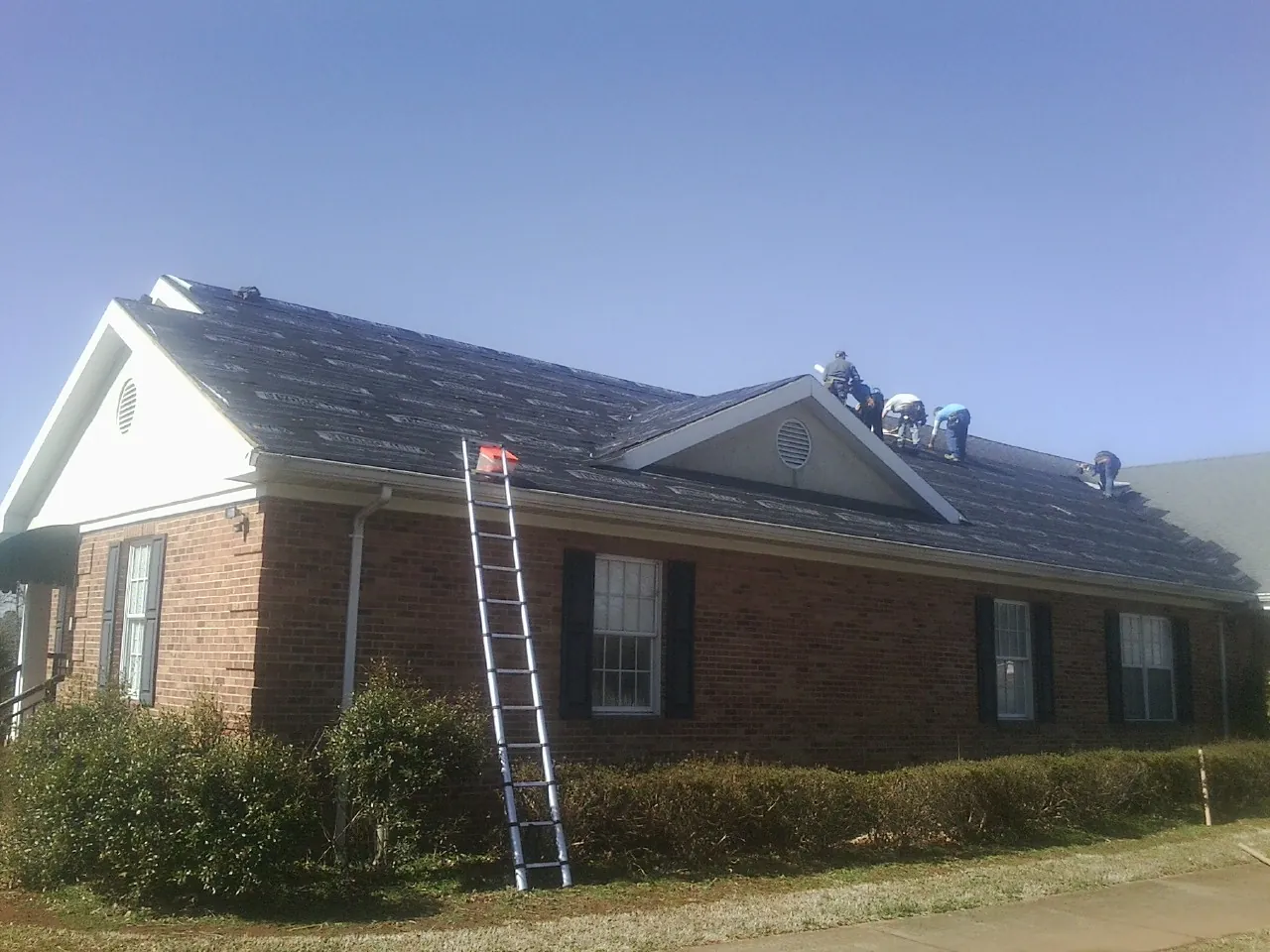 Crew tearing shingles off a brick ranch roof with a ladder set — Emergency Roof Repair work by our crew in Islandia
