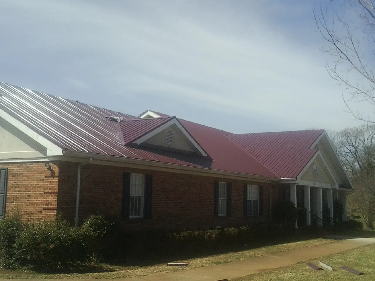 Red metal roof with gabled entries on a long brick building, from a Hail Damage Roof Repair job in Islandia