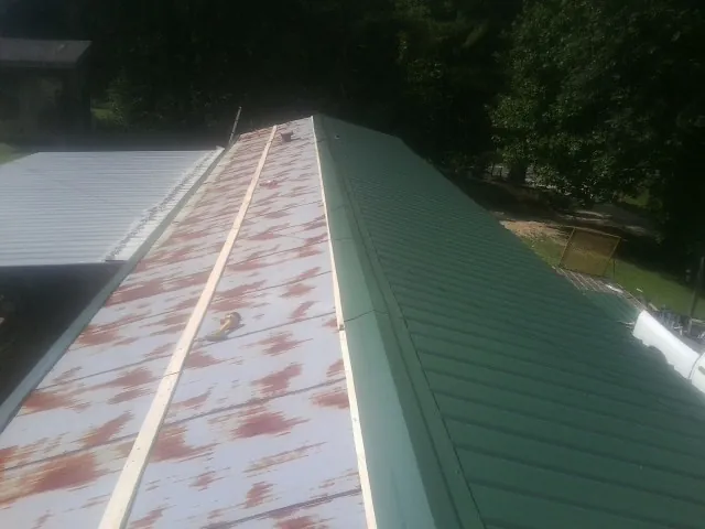 Old rusted panels beside newly installed green metal roofing — Wind Damage Roof Repair by Roofing Brothers in Islandia