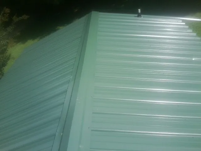 New green metal panels meeting at the ridge of a roof — Flat Roof Repair work by our crew in Islandia