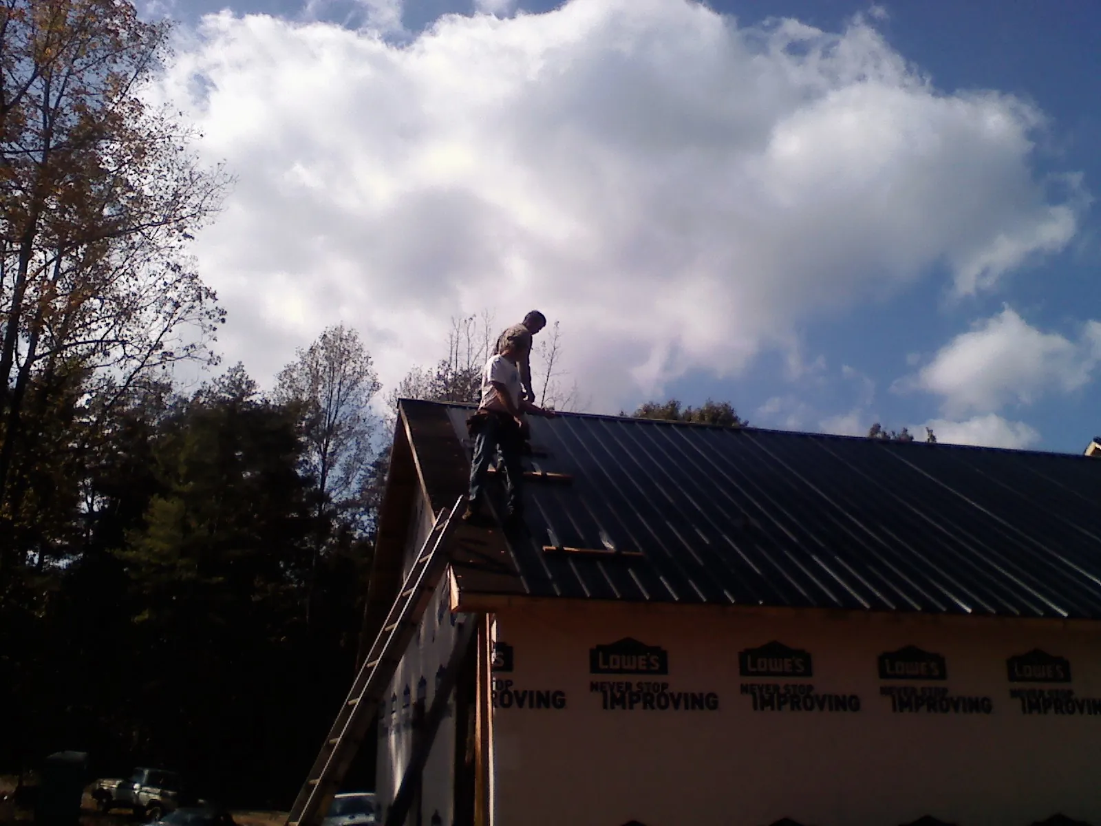 Roofer fastening dark metal panels high against a cloudy sky, from a Roof Inspection job in Islandia