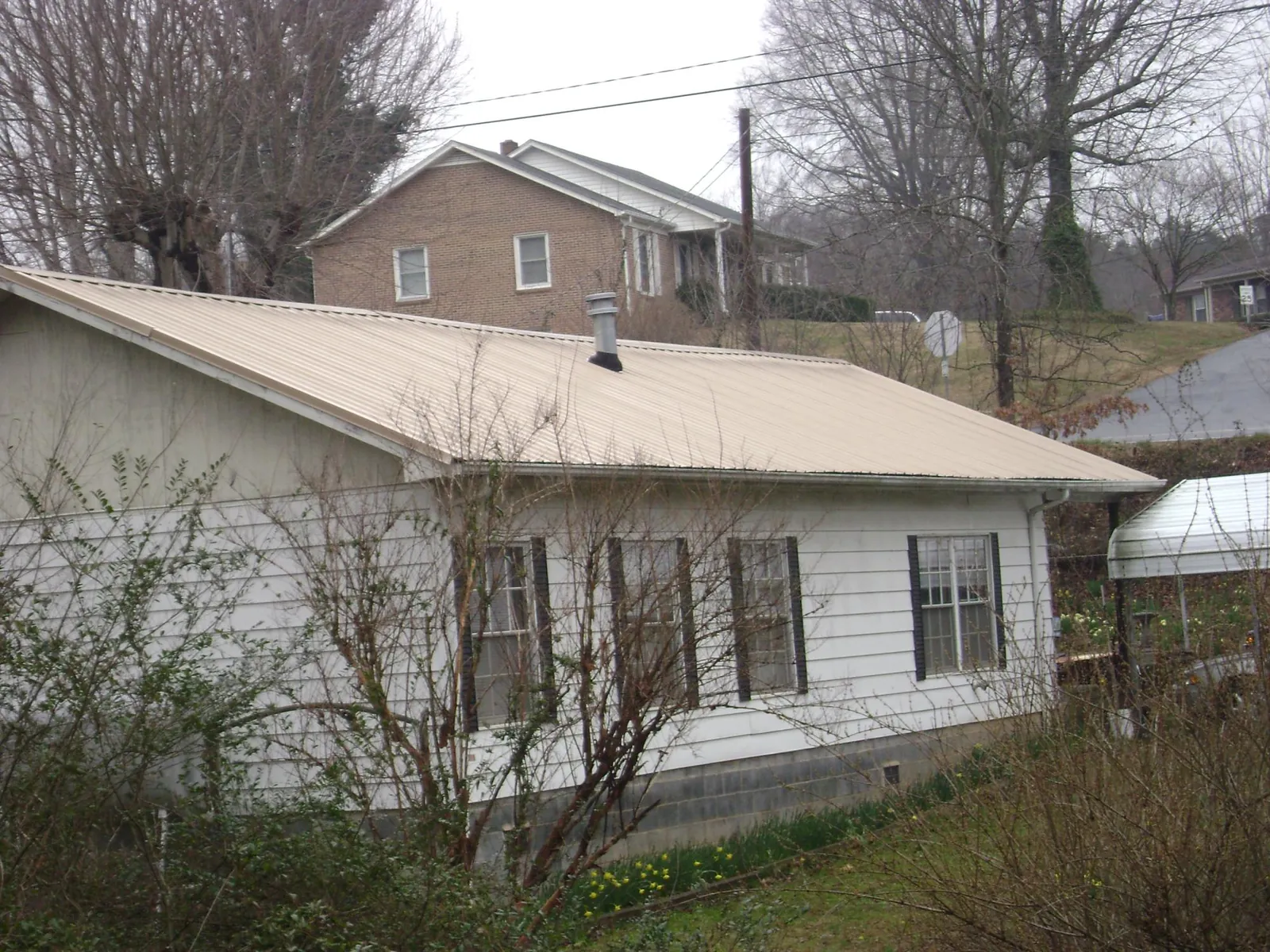 Tan metal roof on a white sided house set into a hillside — Commercial Roofing by Roofing Brothers in Islandia